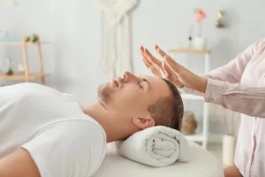 Manos de un terapeuta Reiki sobre su paciente. El Reiki alivia estrés, reduce ansiedad, dolor crónico, mejora el sueño y promueve bienestar emocional y espiritual, equilibrando las energías del cuerpo.